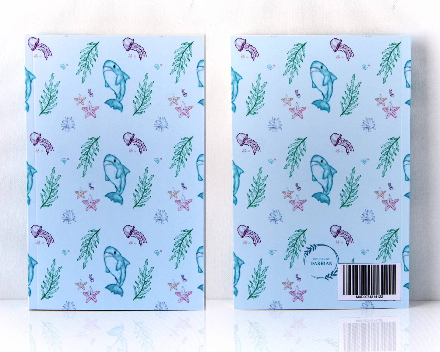 Front and back of a pastel blue notebook with a watercolour pattern featuring sharks, jellyfish, starfish, shells, and seaweed.