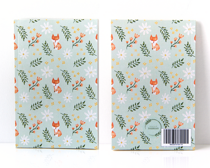 front and back of a notebook with a sage green cover featuring a watercolour pattern with orange foxes, daisies, orange and yellow flowers, and leaves.