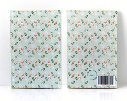 front and back of a notebook with a sage green cover featuring a watercolour pattern with orange foxes, daisies, orange and yellow flowers, and leaves.