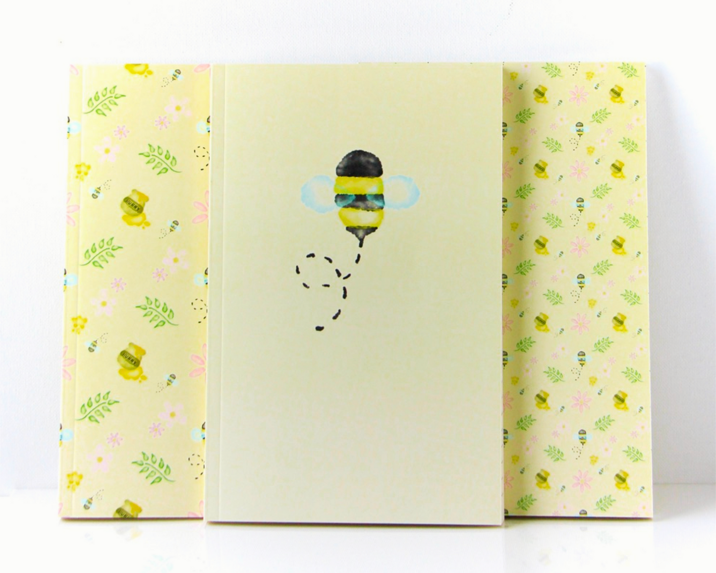 Yellow Pastel Notebook Set of Three with covers featuring watercolour bees, leaves, pink flowers, and honey pots